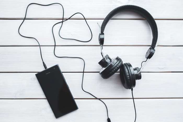 Black headphones connected to a smartphone on a white wooden surface