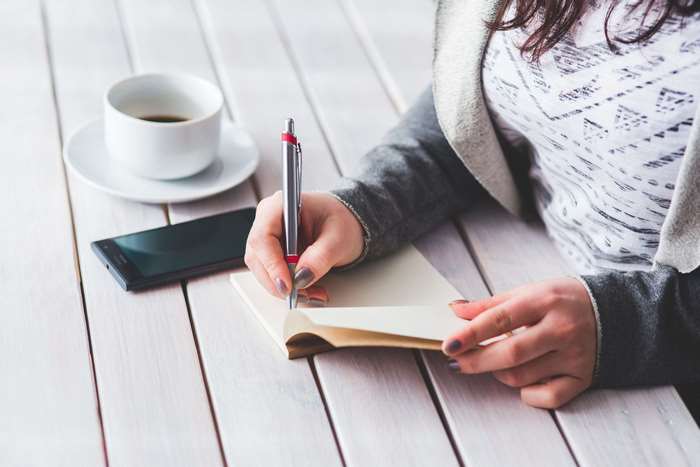 Woman writing in notebook with coffee and phone