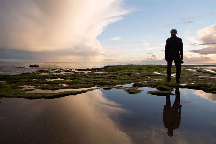 Man standing on mossy rocks with reflection in water