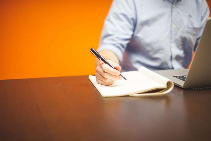 Man writing in notebook at desk with laptop
