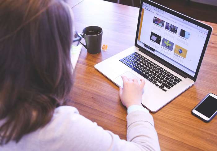 Woman using Apple MacBook and iPhone on wooden desk