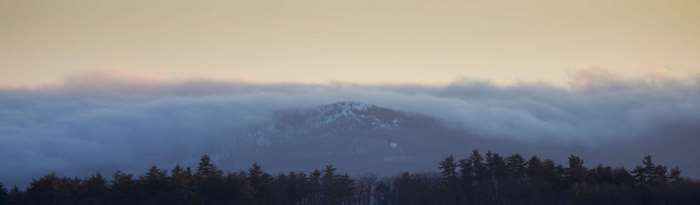 Mountain peak emerging from clouds above forest