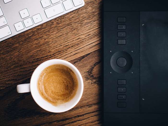 Coffee cup, keyboard, and drawing tablet on a wooden desk