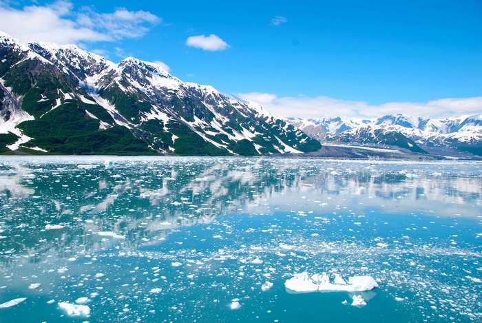 Glacier and snow-capped mountains reflecting in icy water under blue sky