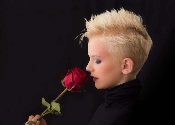 Young woman with blonde hair smelling a red rose