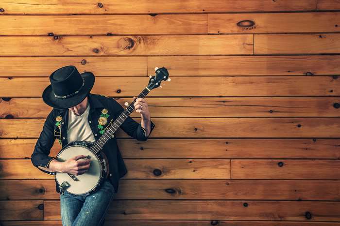 Man in hat playing banjo against wood paneling