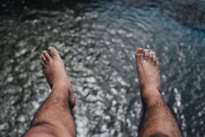 Male hairy legs and feet over water