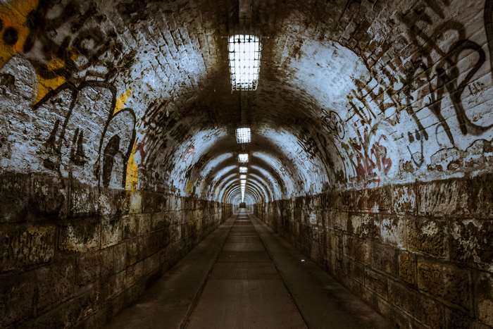 Graffiti-covered brick tunnel with lights