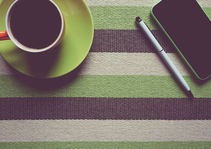 Coffee cup, pen, and smartphone on striped surface