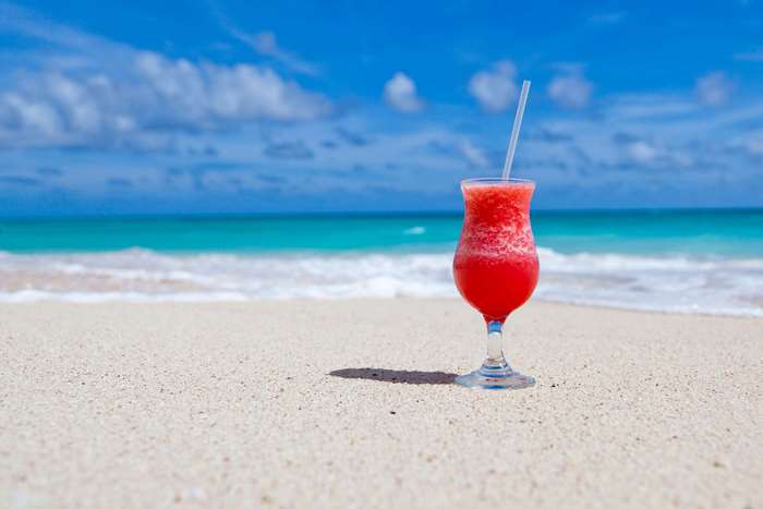 Red cocktail on a sandy beach with ocean background