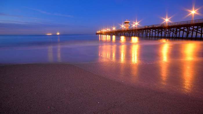 Pier with lights reflecting on water at dusk