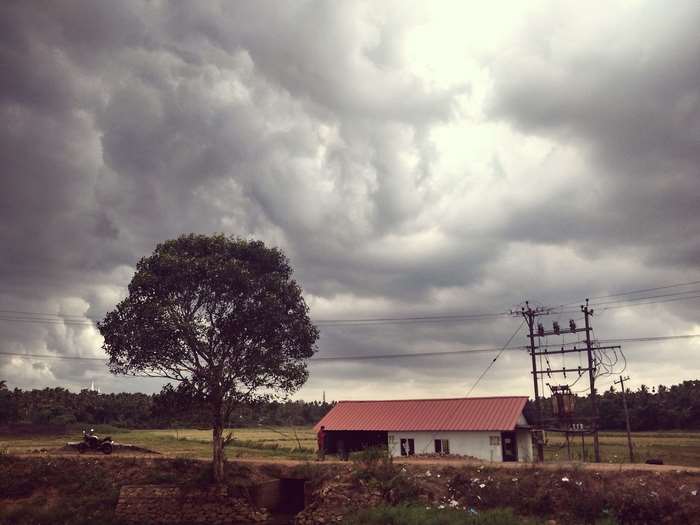 Dark monsoon clouds over a rural landscape with a house and tree