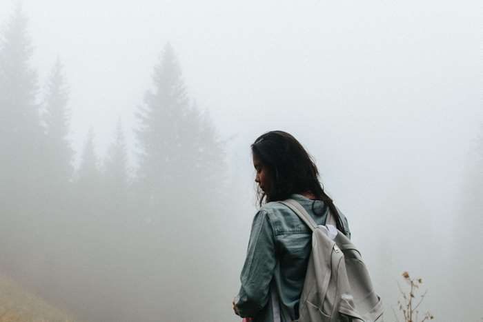 Girl with backpack in foggy forest