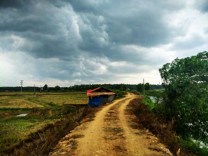 Dirt road leading to a small hut under dark monsoon clouds