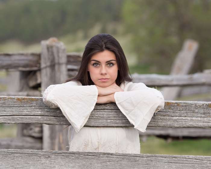 Young woman leaning on a wooden fence outdoors