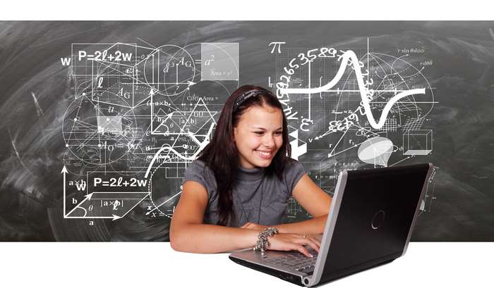 Girl studying mathematics on a laptop in front of a blackboard with formulas