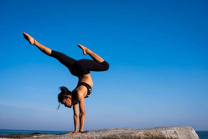 Woman performing yoga handstand on rock by the sea