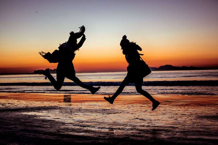 Two people jumping on a beach at sunset
