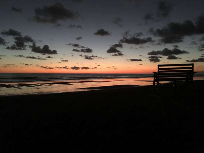 Bench on a beach at sunset with clouds and ocean