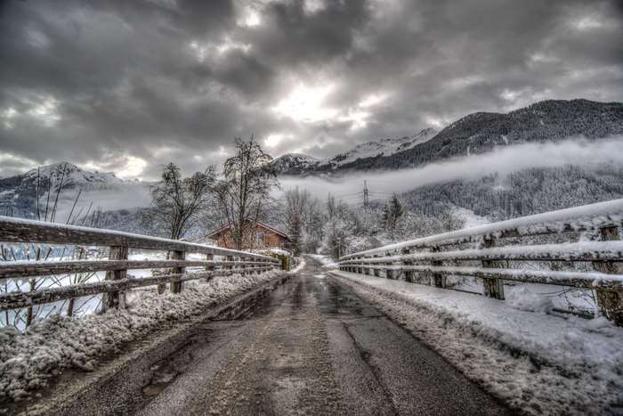 Snowy bridge over a road with mountains and clouds