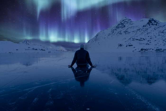 Person sitting on ice watching Northern Lights
