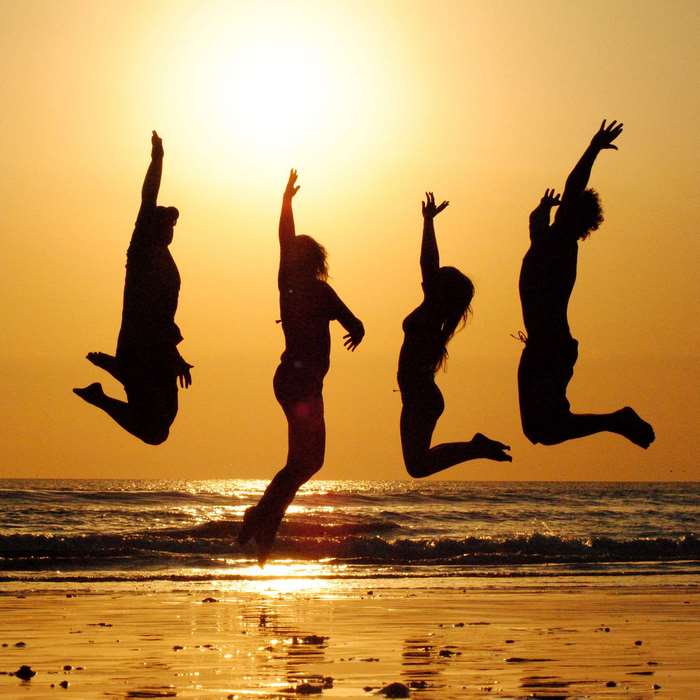 Silhouettes of four friends jumping on a beach at sunset