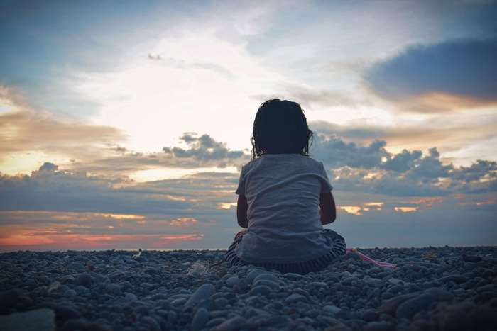 Child sitting on pebble beach at sunset 4K