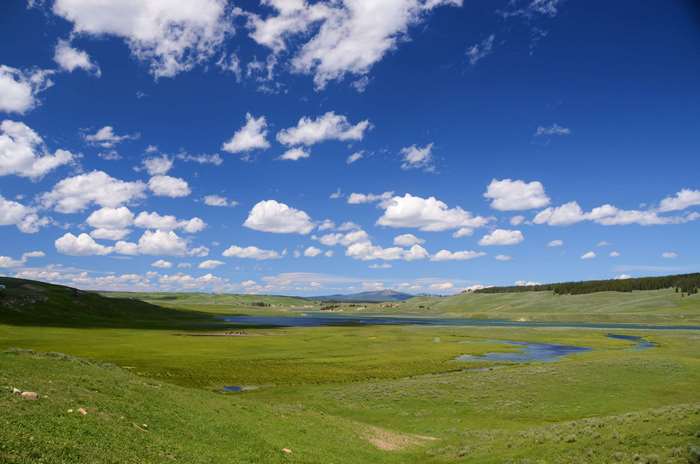 Green hills and lake under a blue sky with clouds