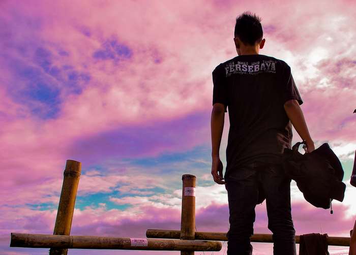 Man standing by bamboo fence at sunset