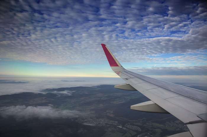 Airplane wing flying over clouds and landscape