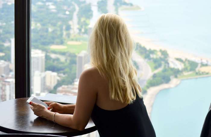 Woman with blonde hair looking out window at city and lake