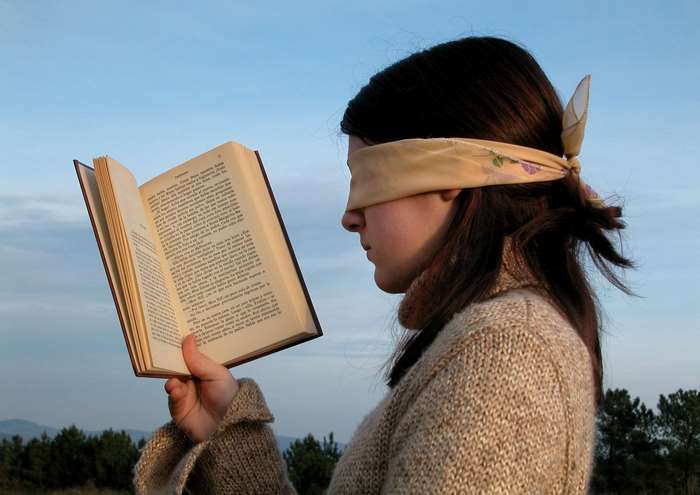 Woman blindfolded reading a book outdoors