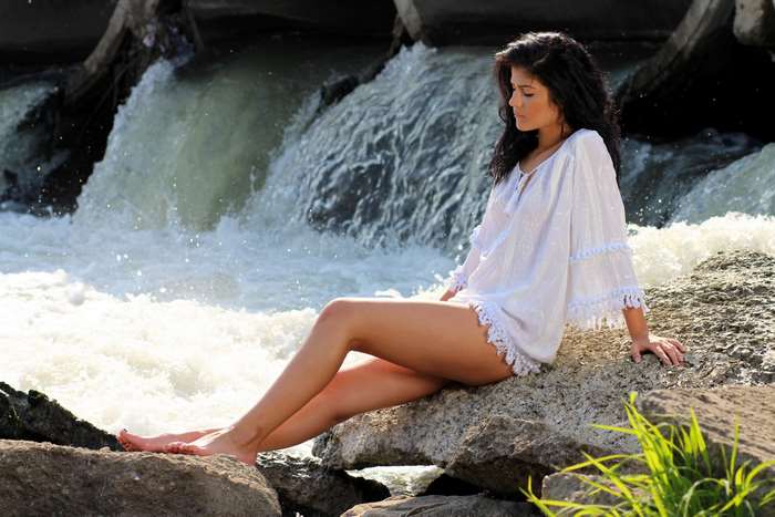 Woman in white dress sitting on rocks by waterfall