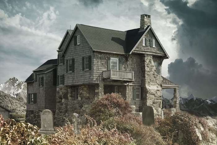 Haunted house on a hill with tombstones and mountains