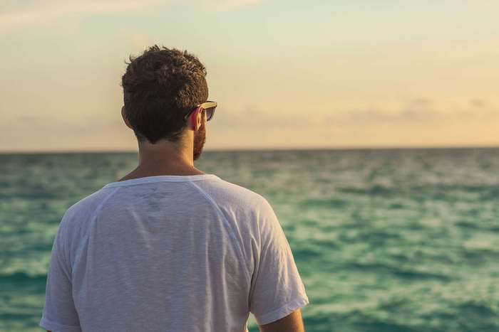 Man in white t-shirt looking at the ocean at sunset
