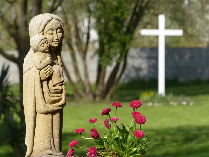 Statue of Virgin Mary holding Child Jesus with cross in background