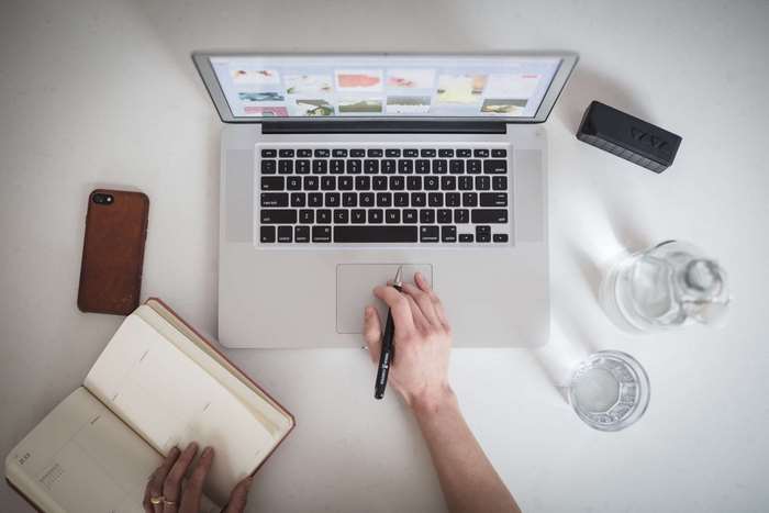 Overhead view of a person working on a MacBook with a notebook and smartphone