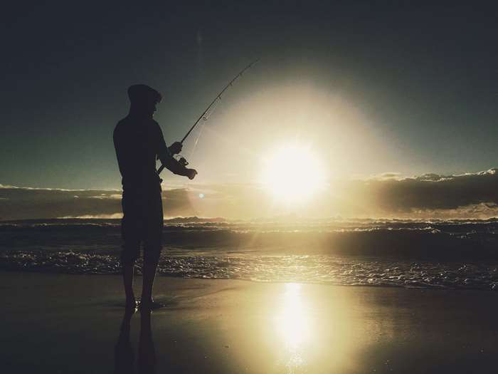 Man fishing on beach at sunrise 4K