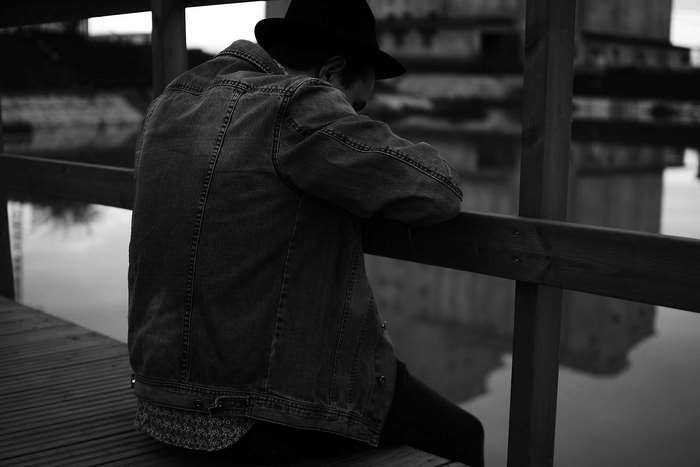 Man in denim jacket and hat sitting by water
