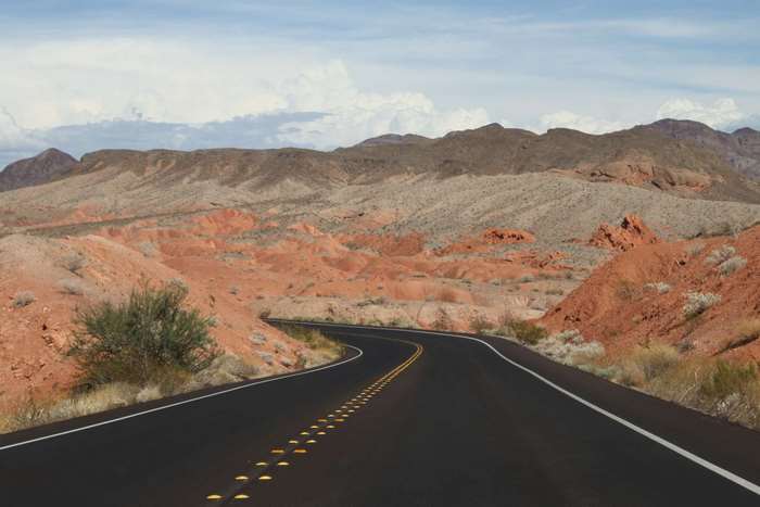 Desert highway winding through red rock mountains under a cloudy sky