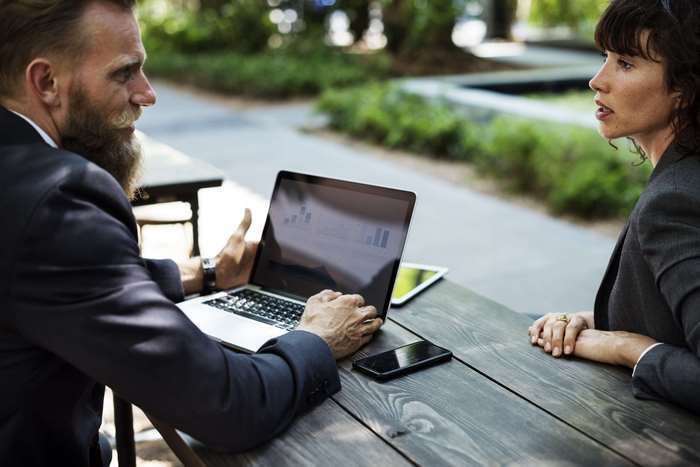 Man and woman in business attire discussing a laptop presentation outdoors