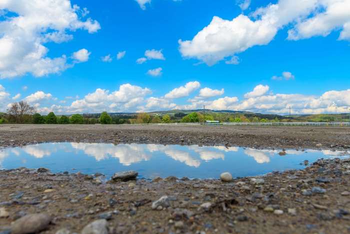Puddle reflecting blue sky and clouds on a dirt ground
