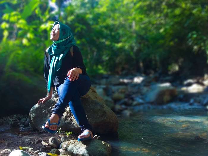 Young woman wearing hijab sitting by a river in a forest