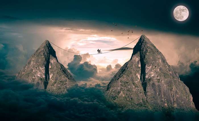 Couple cycling on a tightrope between mountains under the moon