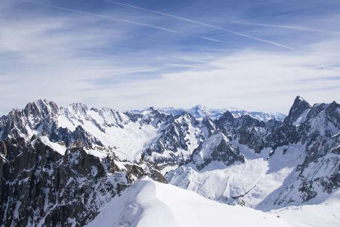 Snow-covered mountains under a blue sky with contrails