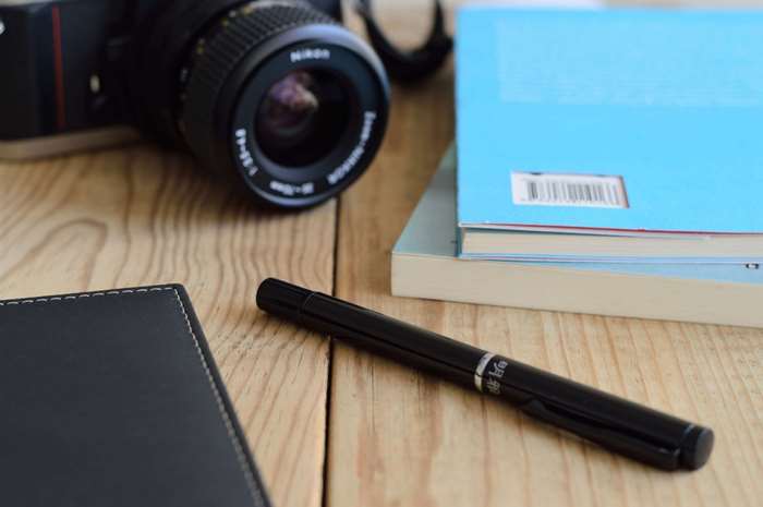 Nikon camera, books, pen, and notebook on a wooden table
