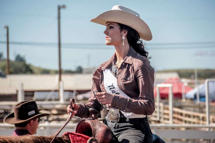 Cowgirl wearing a sash rides a horse at a rodeo