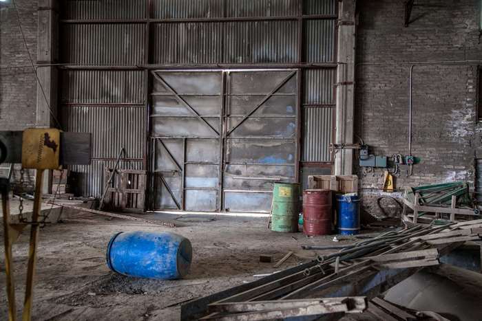 Abandoned warehouse interior with large metal doors and barrels