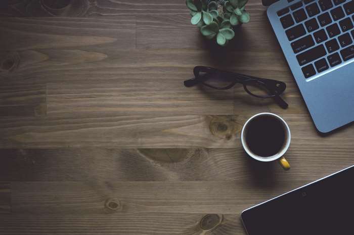 Laptop, coffee cup, glasses, and plant on wooden desk
