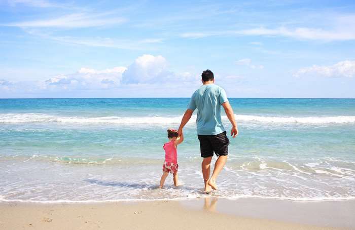 Father and daughter walking on a sunny beach by the sea